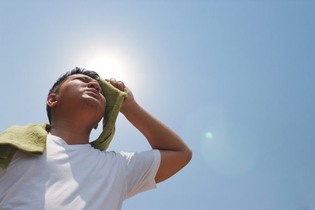 A man wipes his brow in the hot sun