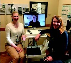 Two providers sit at a TeleHealth (TV Monitor) with a patient onscreen