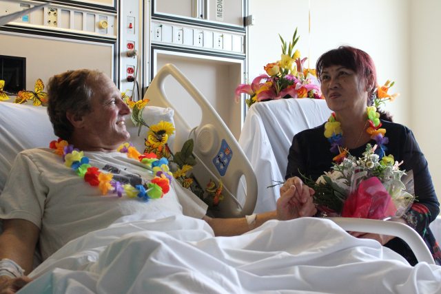 A couple in a hospital room, one a patient, with leis around their necks  in discussion