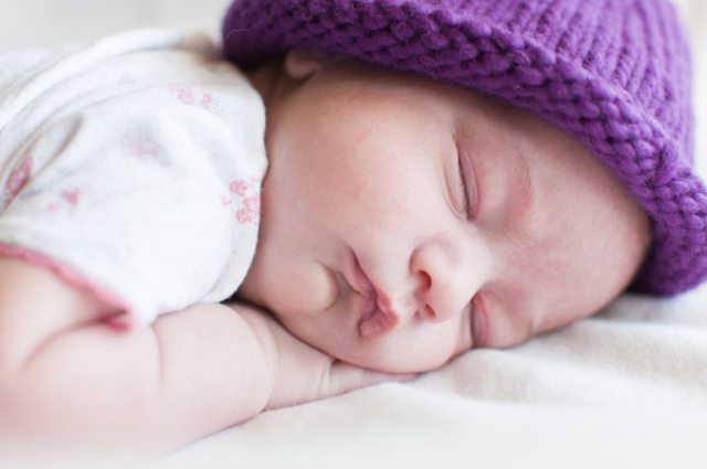 A newborn in a purple knitted hat sleeping