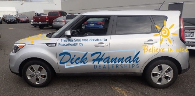 Silver Kia with illustration and words on the side that read "Dick Hannah Dealerships - Believe in Nice"