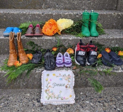 Shoes and flowers placed on a steps in remembrance, with a pillow that reads "Peace"