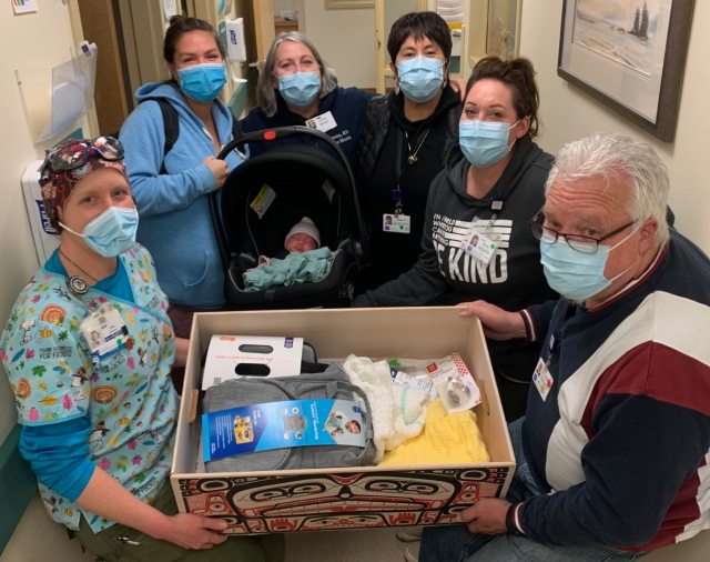 A group of masked healthcare providers escorting a newborn and all of the necessary supplies as they leave the hospital/