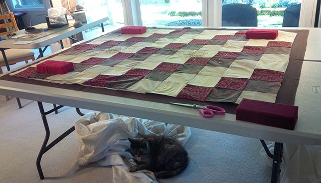 Beth's cat, Jasmine, cuddles under the table laid out with Beth's next quilt top. 