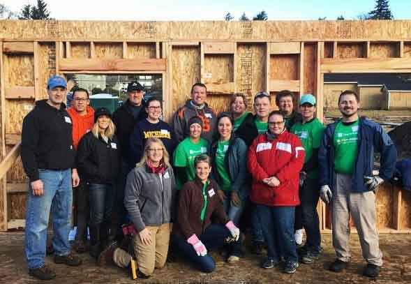 A volunteer group with Habitat for Humanity poses for a photo next to the house they're building
