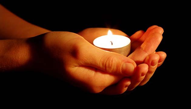hands holding a lit candle in memory of someone lost