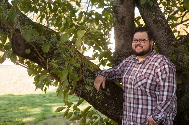 A man stands next to a tree while smiling