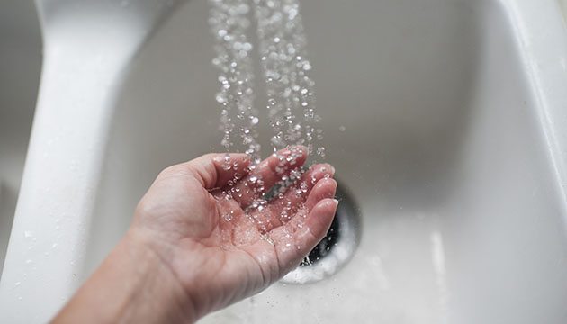A person's palm held under running water over a sink