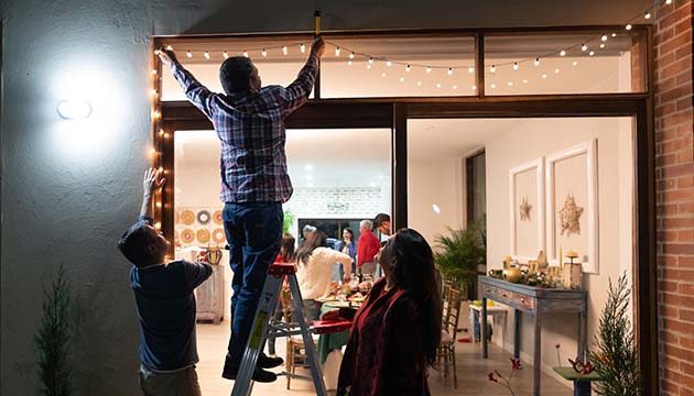 three people hang Christmas lights on house