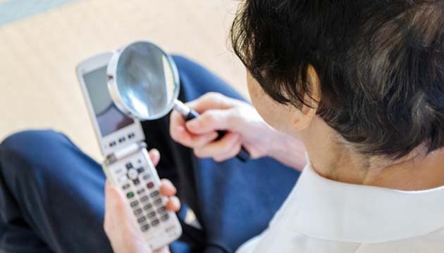 woman uses magnifying glass to read screen of mobile phone