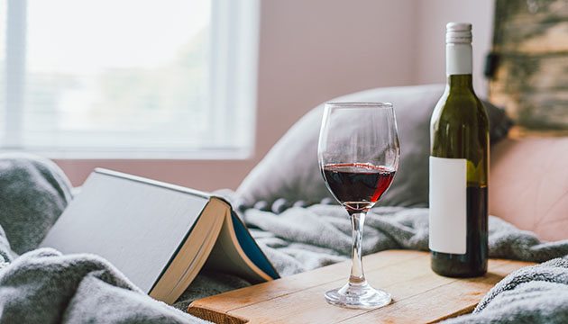 Glass of red wine next to a bottle and open book