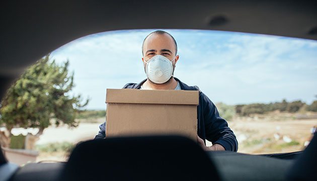 Man wearing a mask pulls boxes out of his car