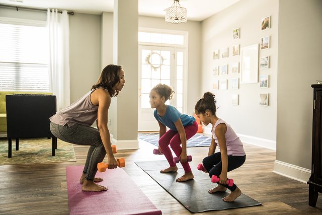 Woman exercising indoors with two young children.