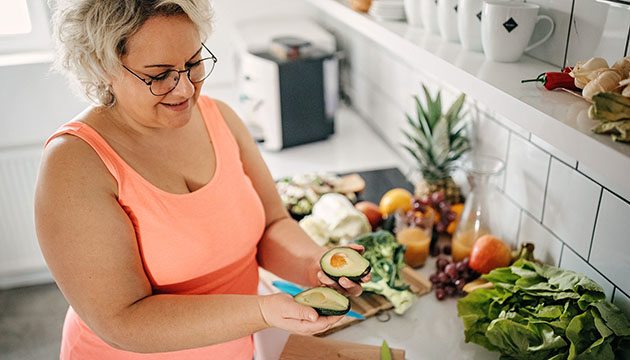 Woman opens a sliced avocado in her kitchen
