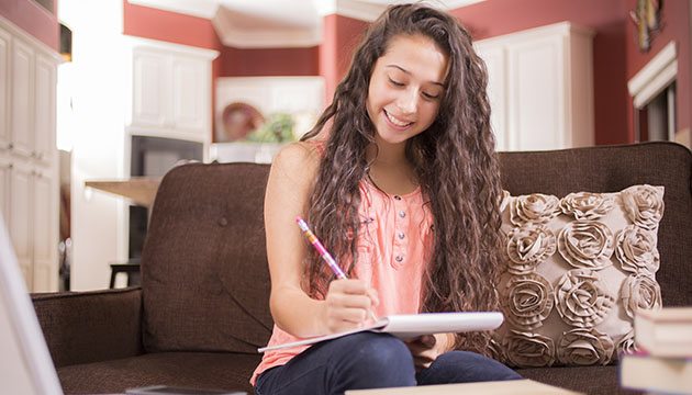 teen girl writing in a notebook at home