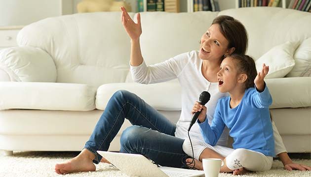 A mom and daughter sit next to a couch and sing karaoke together