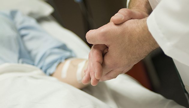 Provider clasps hand of patient in hospital bed