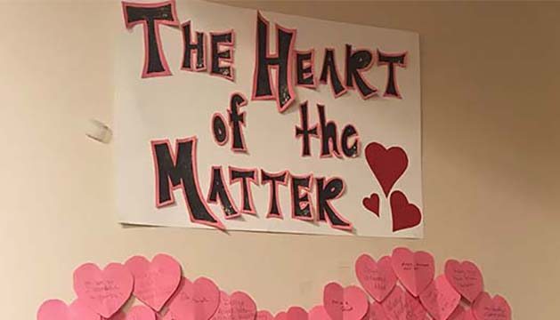 A sign hangs on the wall adorned with hearts and the phrase "The Heart of the Matter" written on it