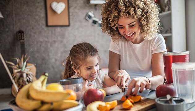 Young girl and young mother cut up fruit in their kitchen
