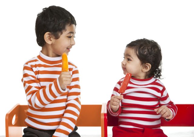 Two children in striped shirts enjoy popsicles