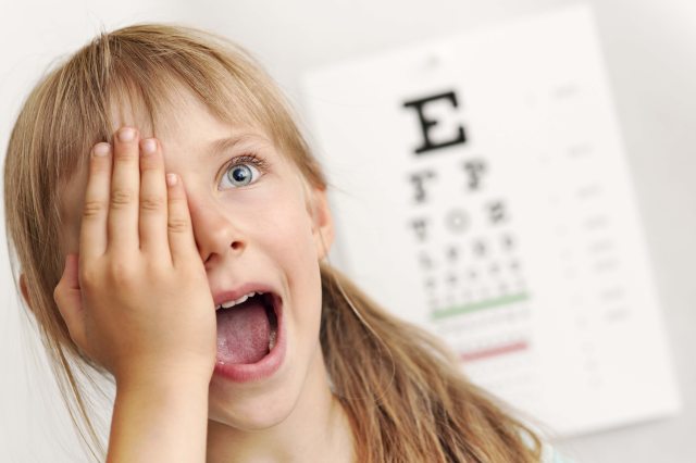 A young child covers one eye while at the eye doctor's office