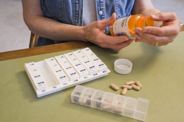 A person reads the label on a prescription bottle with a pill counter and calendar on the table in front of them.