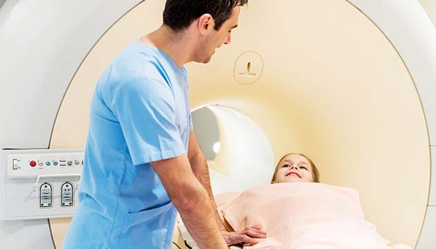 A Child speaks with a healthcare provider while preparing for a scan in an MRI machine