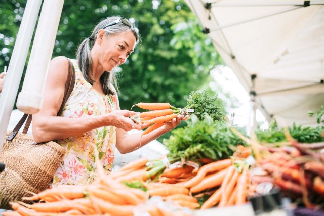 A smiling woman selects a bunch of carrots from a food stand