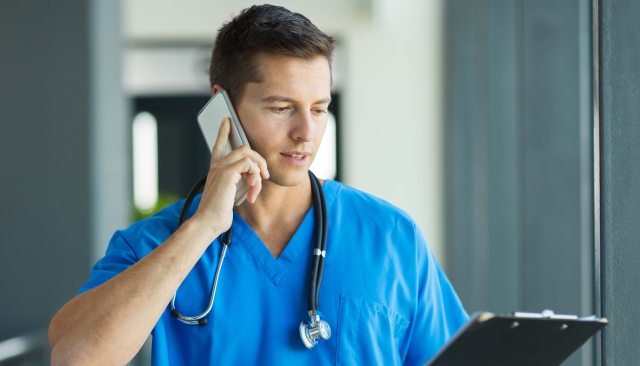 Healthcare provider in scrubs talks on the phone while looking at a patient chart