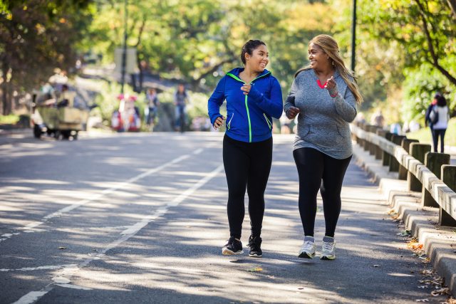 Two women jogging down the street and smiling at each other