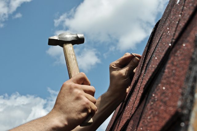 A person hammers nails into a shingle roof