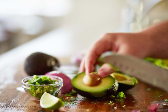 Close-up of a knife cutting an avocado and other vegetables