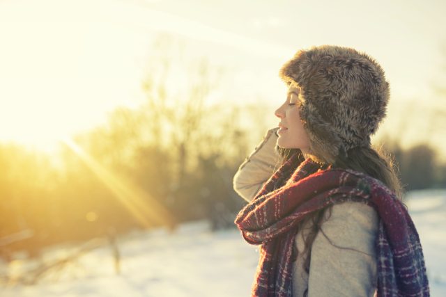A woman in winter clothing on a field of snow feeling the warmth of the sun