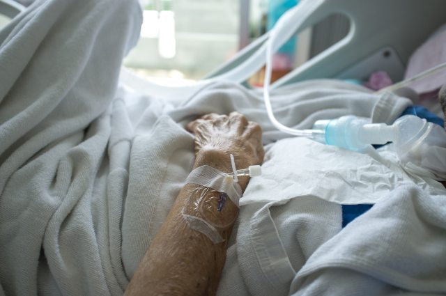 A patient with IV needles taped to their hand rests in a bed
