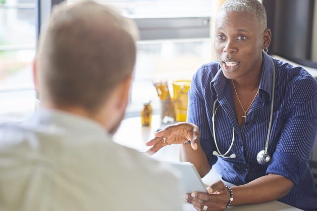 A healthcare provider explains somehting to a patient across a table, while holding notes