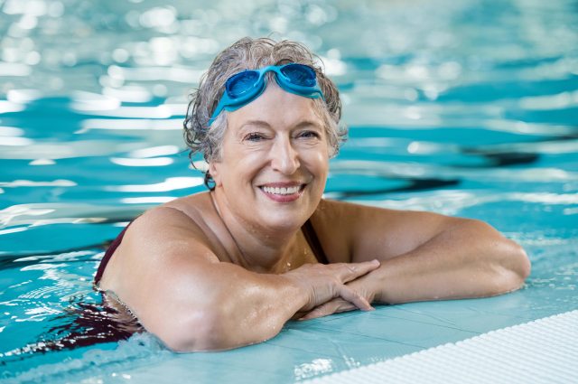 A senior woman smiles while resting on the side of a swimming pool