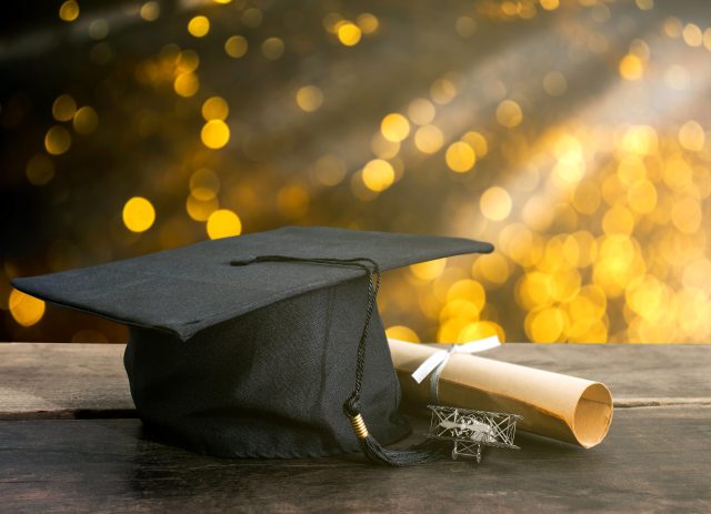 Graduation cap and diploma resting on a table in front of golden light