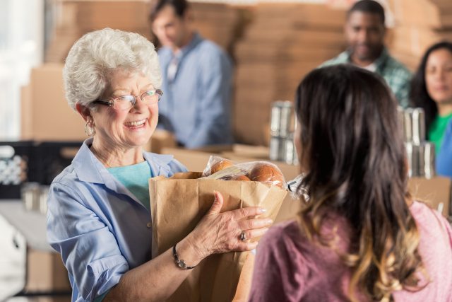 An older woman with a bag of groceries smiles at a person with their back to the camera in the foregorund