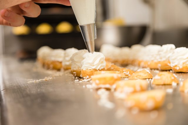 Close-up of baker's hand decorating pastries with whipped cream