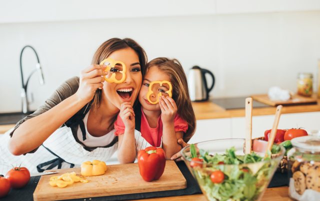 A woman and younger girl hold cut-out sweet bell peppers over their eyes and laugh