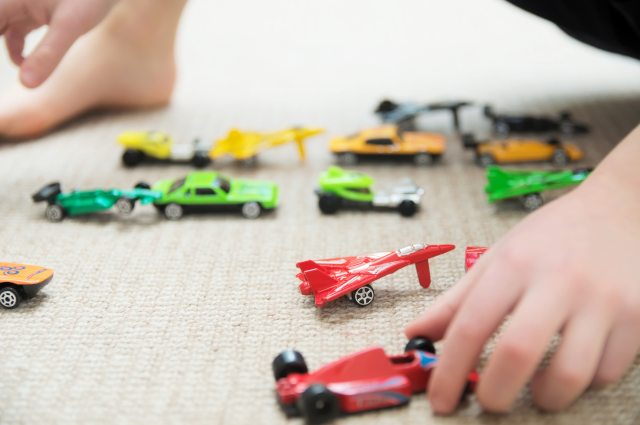 Close-up of young child's hands playing with toy cars and toy airplanes on the floor