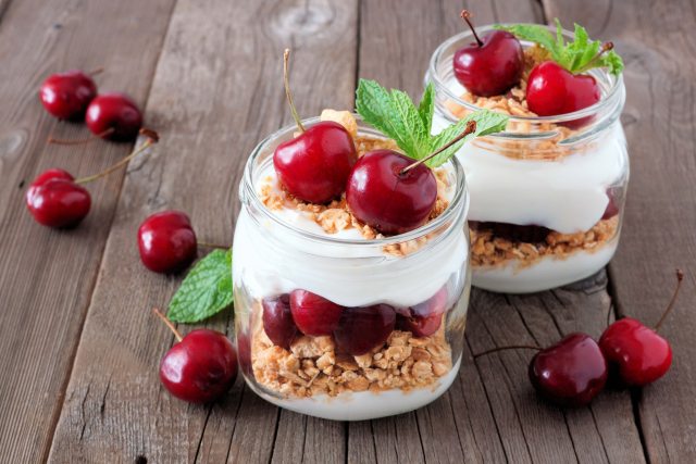2 containers filled with cream, granola and cherries