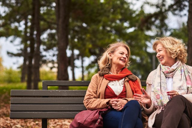 Two women sit on a park bench, smile and chat