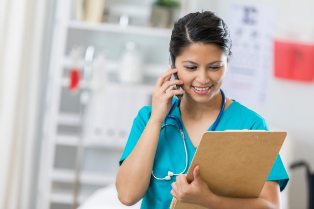 A nurse reading a patient chart and speaking on a phone