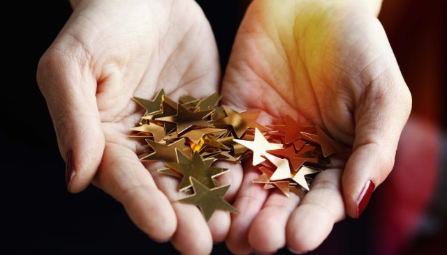 Hands in a cupped shape hold stars that have been cut from foil or gold-colored paper