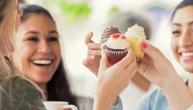 Smiling young women making a toast with frosted cupcakes instead of drinks