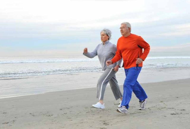 An older couple jogs on the beach next to the ocean
