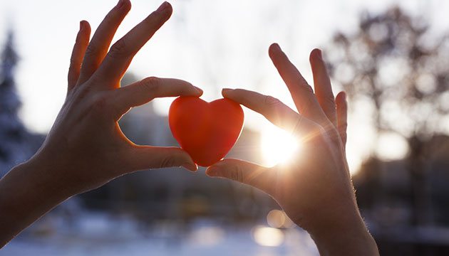 Close-up of hands holding a heart shaped item up to the sunlight