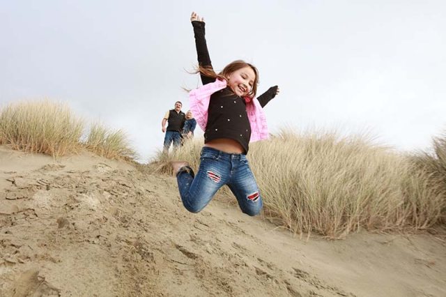 A happy young girl jumps onto beach from sand dune with arms outstretched 