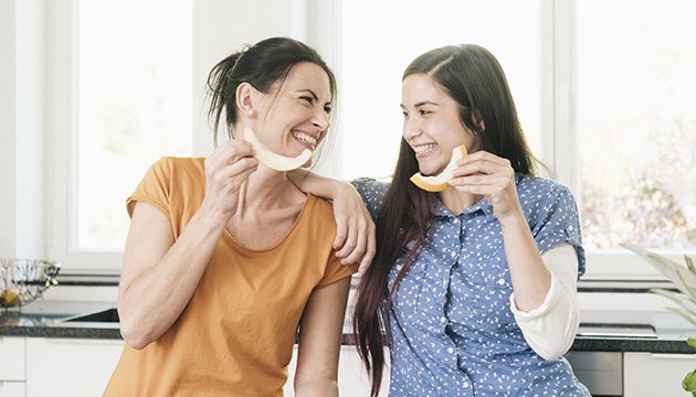 two women smile at each other as they enjoy fruit